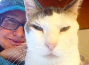 Close up of rescued white stray Dubai street cat with gray markings sitting with woman wearing a blue hoodie